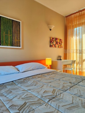 Een hotelkamer met een bed, een bureau, een stoel, een lamp en kunstwerken aan de muren.
