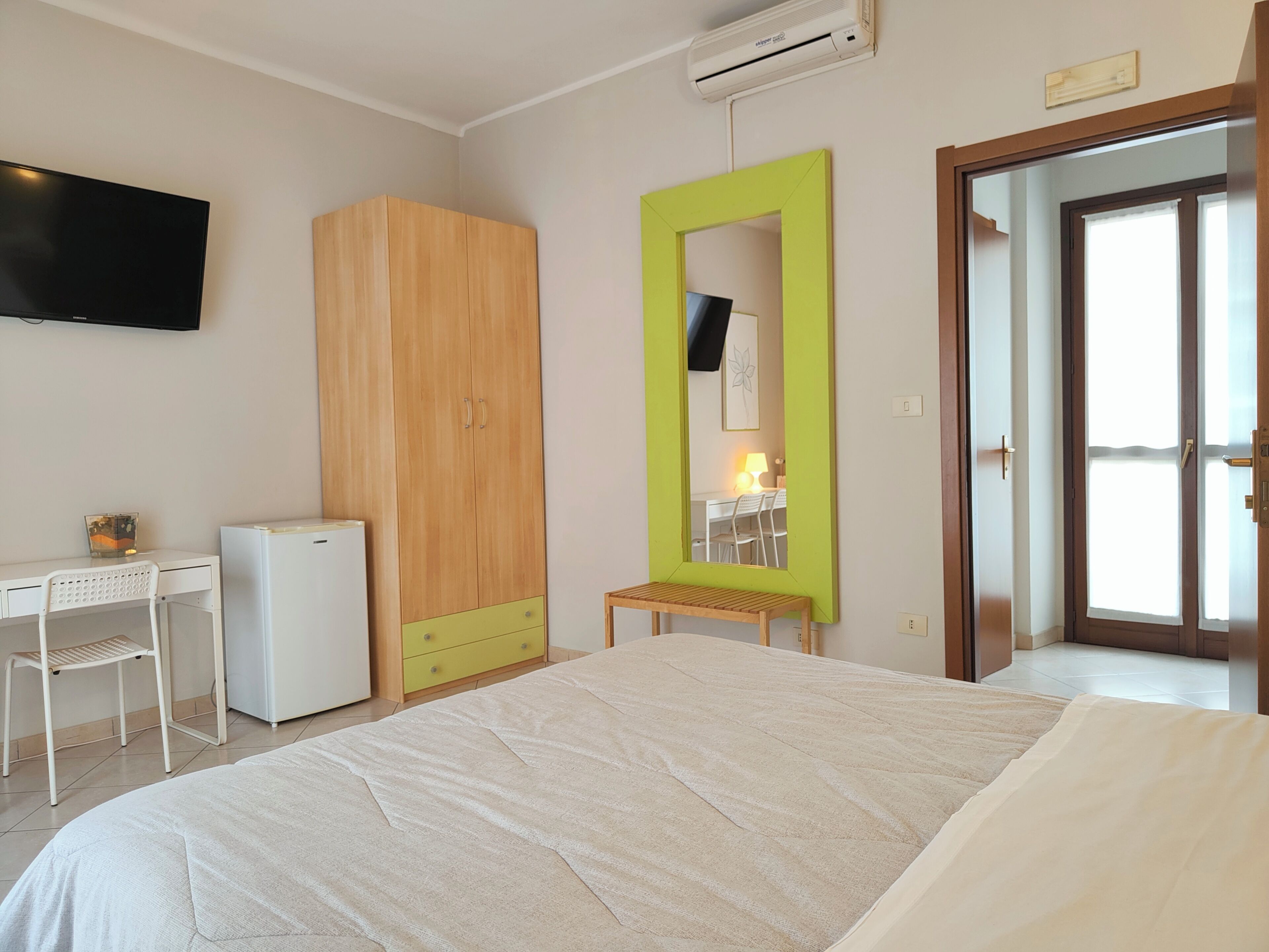 Une chambre à coucher avec un lit, un bureau, une armoire, un miroir et une porte.