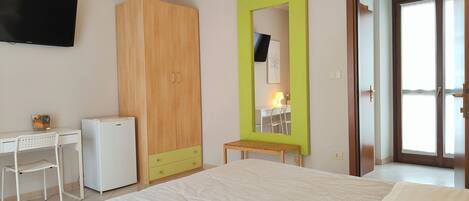 Une chambre à coucher avec un lit, un bureau, une armoire, un miroir et une porte.