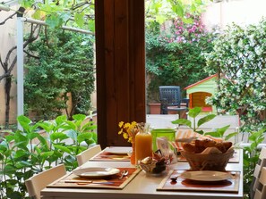 A table set for two with plates, cutlery, a glass of orange juice, a basket of bread, and a vase with flowers. - Torino Guest House (Turin)