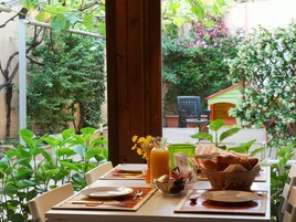 Una tavola imbandita per due, con piatti, posate, un bicchiere di succo d'arancia, un cestino di pane e un vaso di fiori.