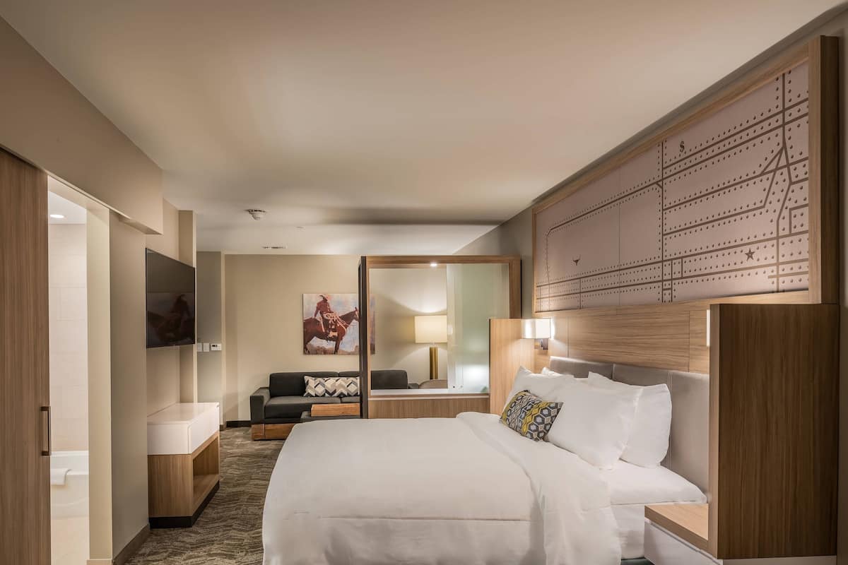 Ein Hotelzimmer mit einem großen Bett, einem Schreibtisch, einem Sessel, einer Couch, einem Fernseher und einem Spiegel.