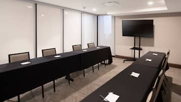 A conference room with a long table, chairs, a flat-screen TV, and a projector.