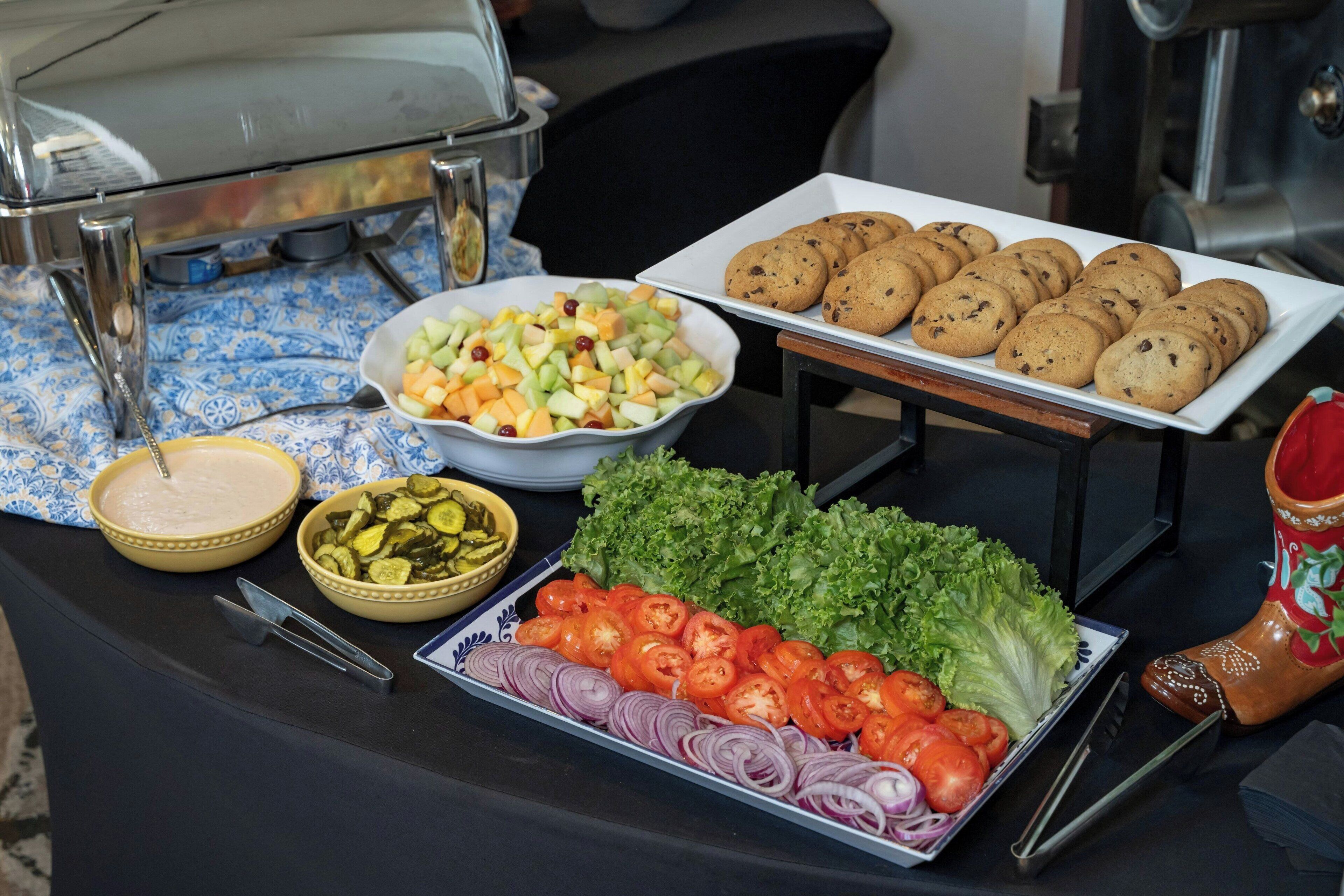 A buffet table with various food items including a salad, cookies, and sliced vegetables.