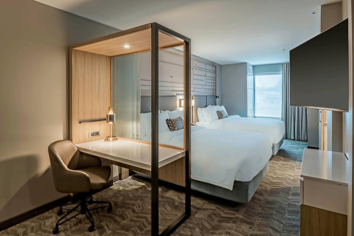 Ein Hotelzimmer mit Bett, Schreibtisch, Sessel, Fernseher und großem Fenster.