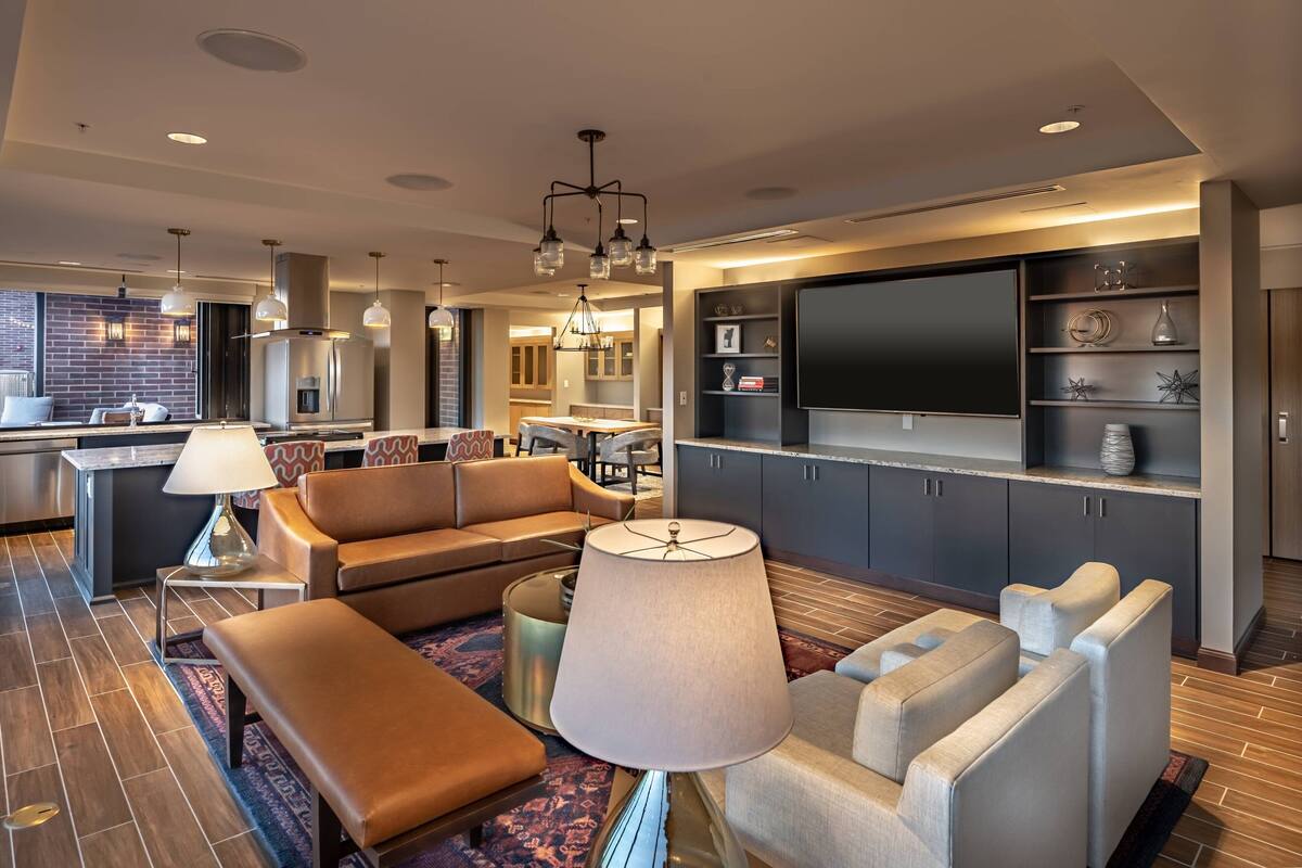Ein modernes Hotelzimmer mit einer Couch, Sesseln, einem Couchtisch, einem Fernseher und einer Küchenzeile.