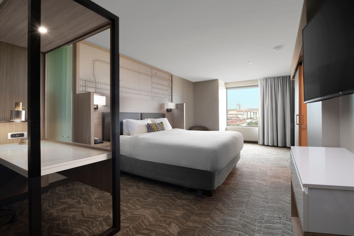 Ein Hotelzimmer mit einem großen Bett, einem Schreibtisch, einem Fernseher und Blick auf die Stadt.