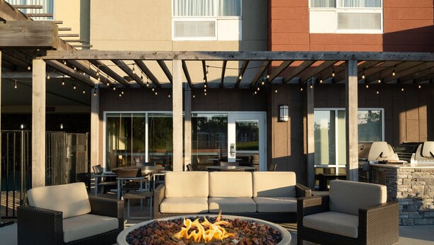 An outdoor patio area with a fire pit, seating, and a pergola with string lights.