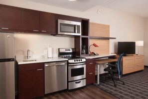 A compact kitchen with a microwave, stove, and refrigerator. There is a small dining area with a table and a chair. - TownePlace Suites by Marriott Lafayette South (Lafayette)