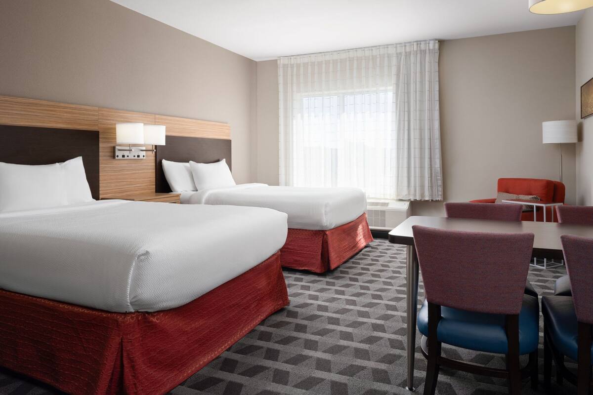 Habitació d'hotel amb dos llits, una taula, una cadira i una finestra amb cortines.