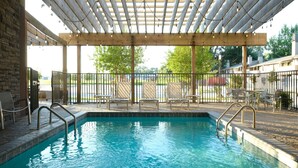 A swimming pool with a pergola overhead, surrounded by chairs and a fenced area.