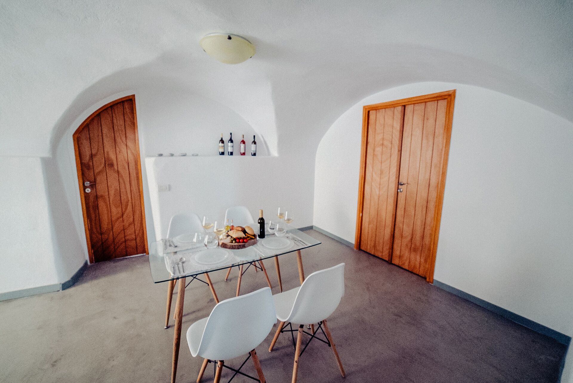 Zona pranzo con tavolo in vetro, sedie bianche e una credenza per vini a parete.