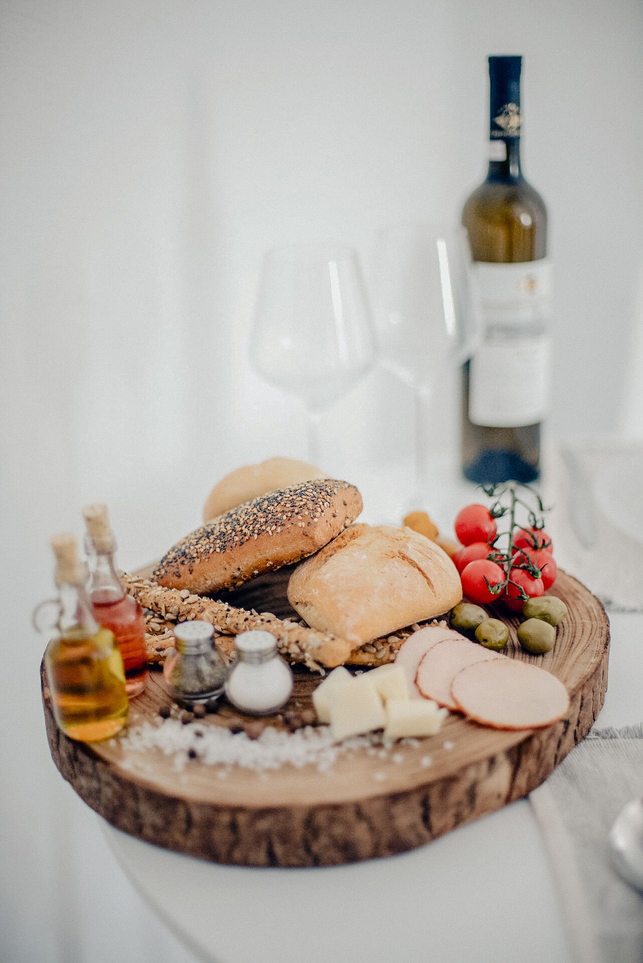 Una tabla de madera con panes variados, quesos, aceitunas y una botella de vino.