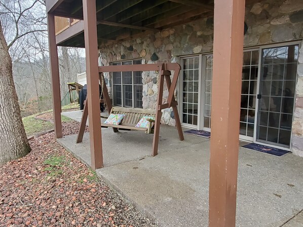 A covered porch with a wooden swing set, stone walls, and a view of a house with large windows. - Private country hillside setting surrounded by trees, birds, wildlife pond/falls (Nashville)