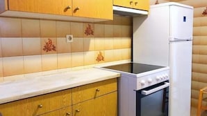 A compact kitchen with wooden cabinets, a white countertop, a built-in oven, and a white refrigerator. - Villa Bagia (Andros)
