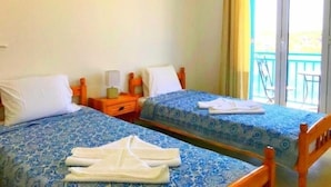 A hotel room with two beds, each with a blue patterned bedspread, white pillows, and a wooden headboard. There is a small table with a lamp and a decorative item between the beds. - Villa Bagia (Andros)