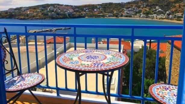 A balcony with a tiled table and chairs, overlooking a coastal town and the sea. - Villa Bagia (Andros)
