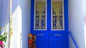 A blue door with decorative glass panels, a small statue, and a blue railing in front. - Villa Bagia (Andros)