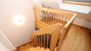 Un escalier en bois avec une rampe, un luminaire fixé au mur et une fenêtre au-dessus.