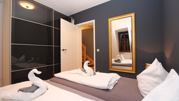 Une chambre d’hôtel avec un grand miroir, une armoire et deux lits garnis de serviettes blanches en forme de cygnes.