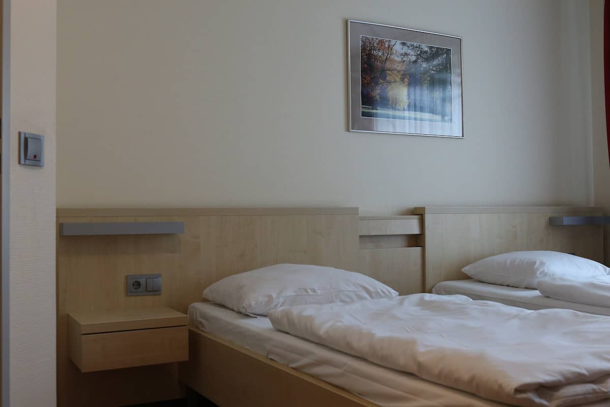 Ett hotellrum med två sängar, en inramad tavla på väggen och ett litet nattduksbord med en lampa.