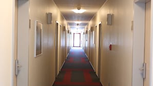A long, narrow hotel corridor with doors on both sides, a red and black carpet, and a ceiling light fixture. - Autohof & Hotel Salzbergen (Salzbergen)