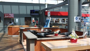 A modern indoor seating area with wooden tables and black leather chairs, a reception desk, and a visible Aral gas station sign. - Autohof & Hotel Salzbergen (Salzbergen)