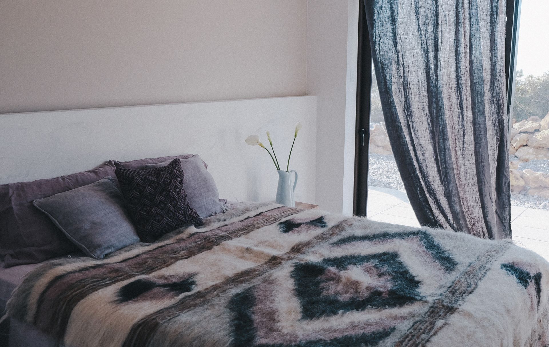A bedroom with a bed, pillows, a blanket, and a vase with flowers.