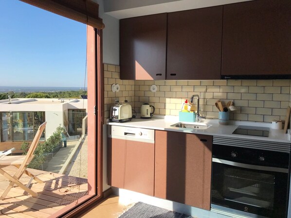 Cocina moderna con horno empotrado, tostadora y hervidor. Hay una puerta corrediza de vidrio que da a un balcón con vistas al paisaje.