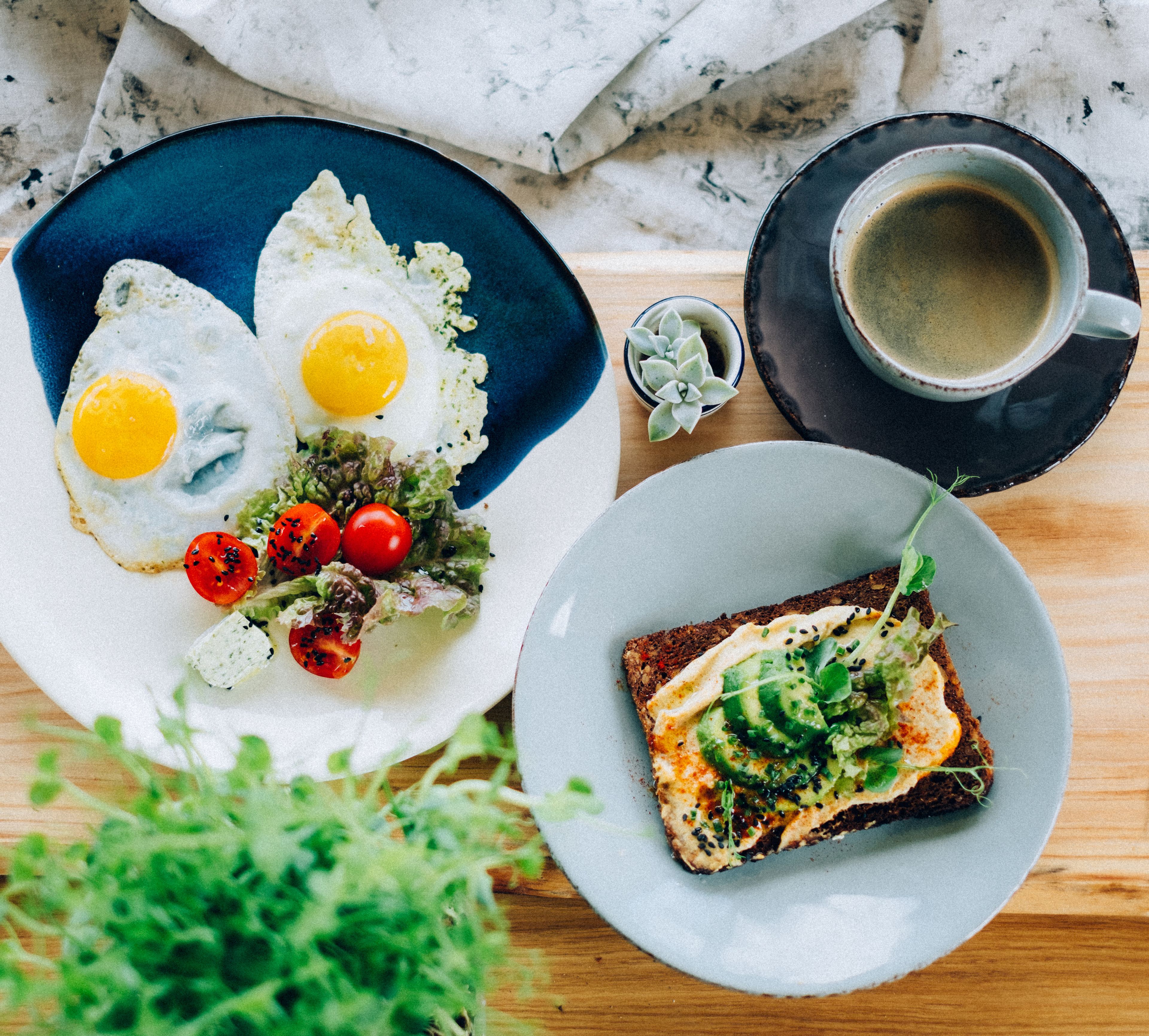 Un desayuno con huevos, tomates y verduras en un plato, una taza de café y una tostada con aguacate y verduras en otro plato.