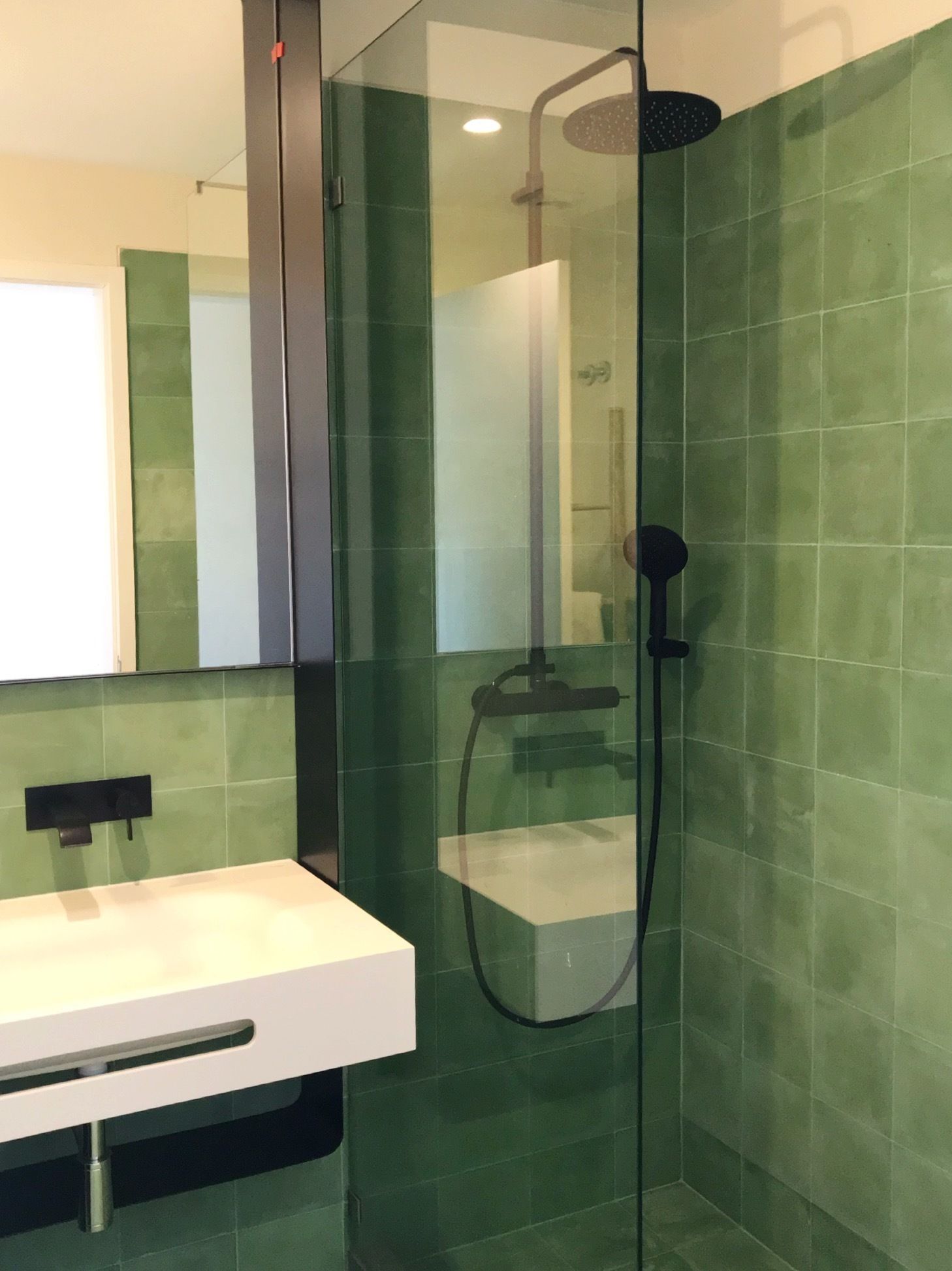 A modern bathroom with a glass-enclosed shower, a white sink, and green-tiled walls.