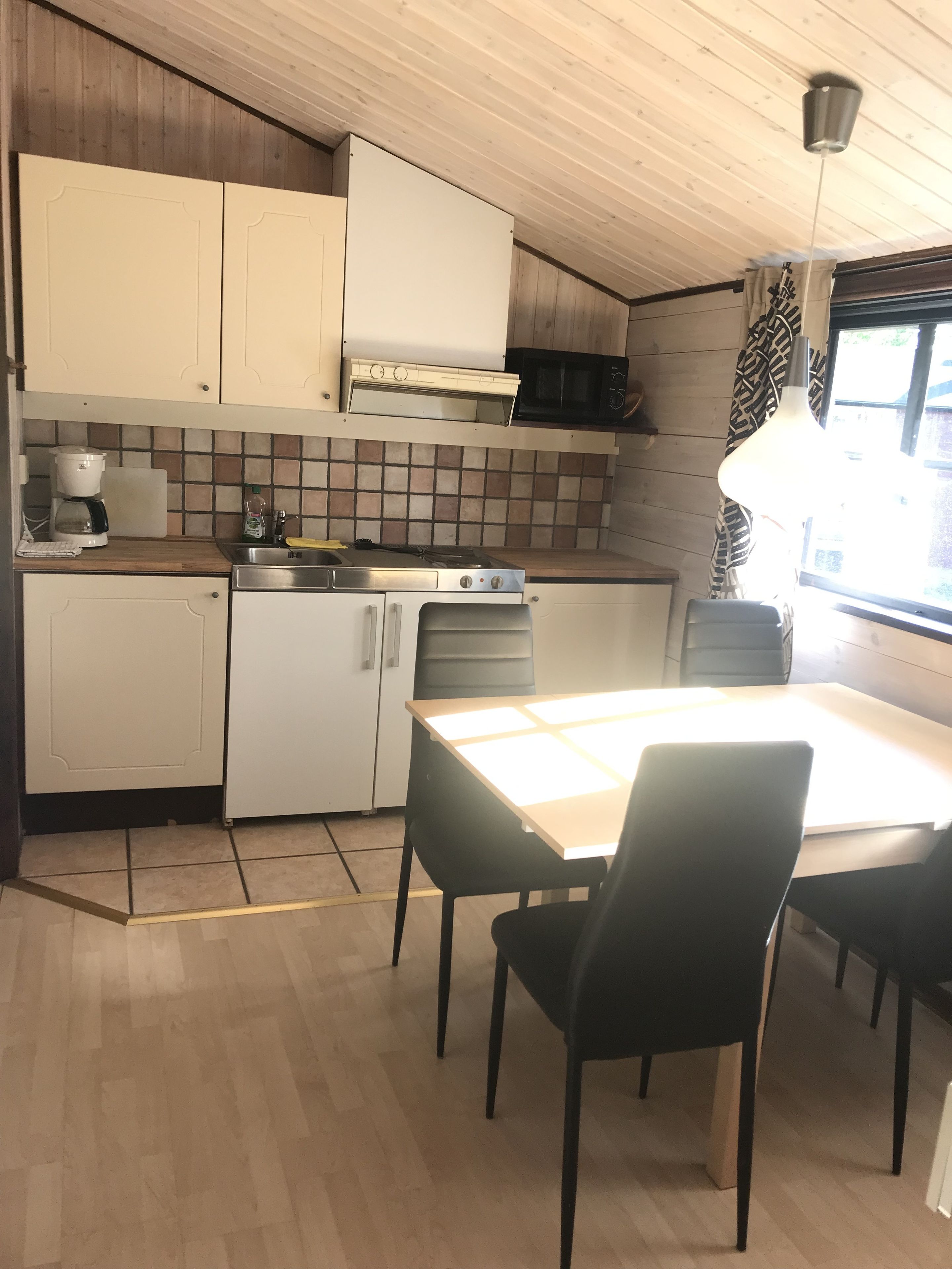Una cocina compacta con armarios blancos, un microondas, una estufa y una mesa de comedor con sillas.
