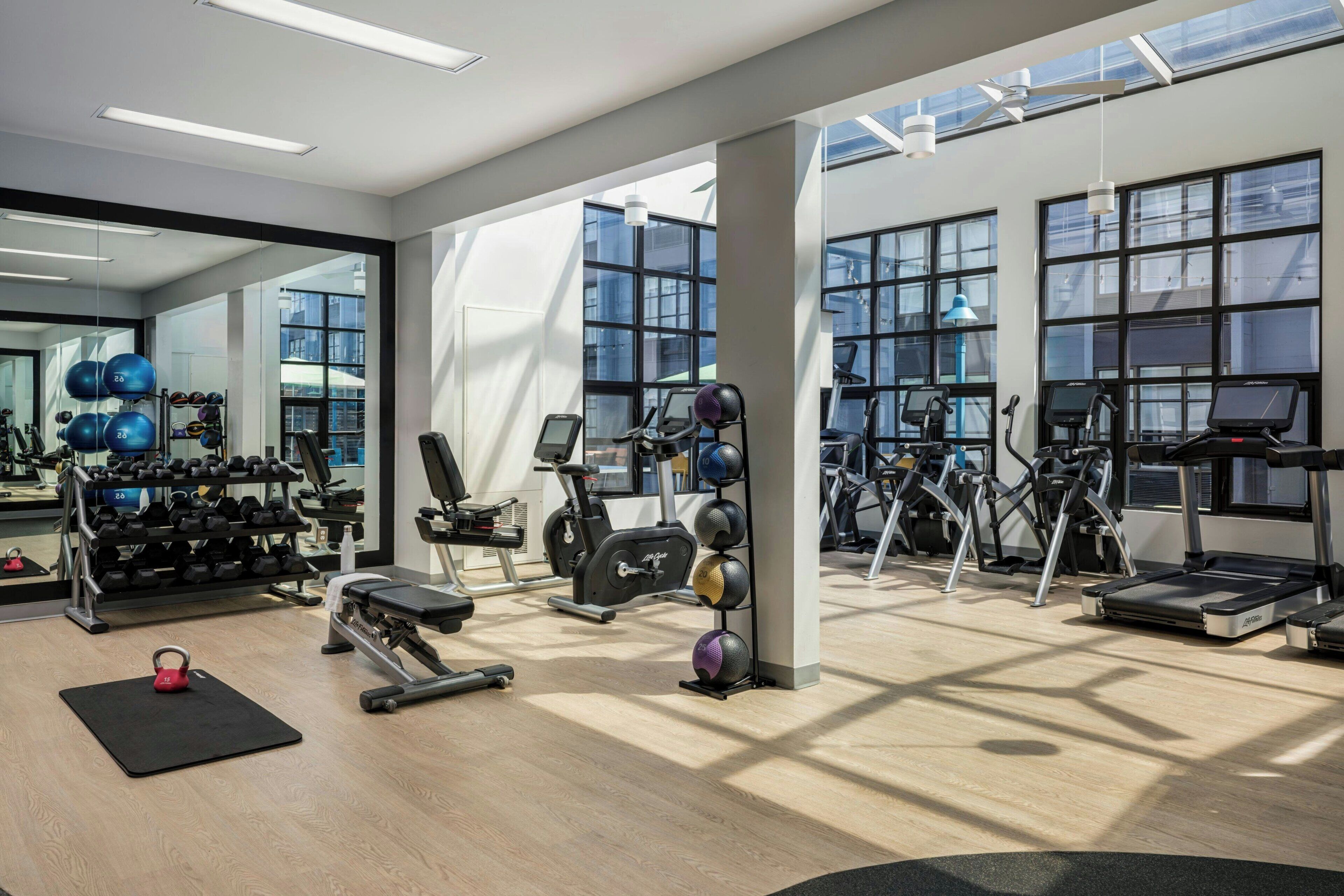 A gym with exercise equipment, a mirrored wall, and large windows.