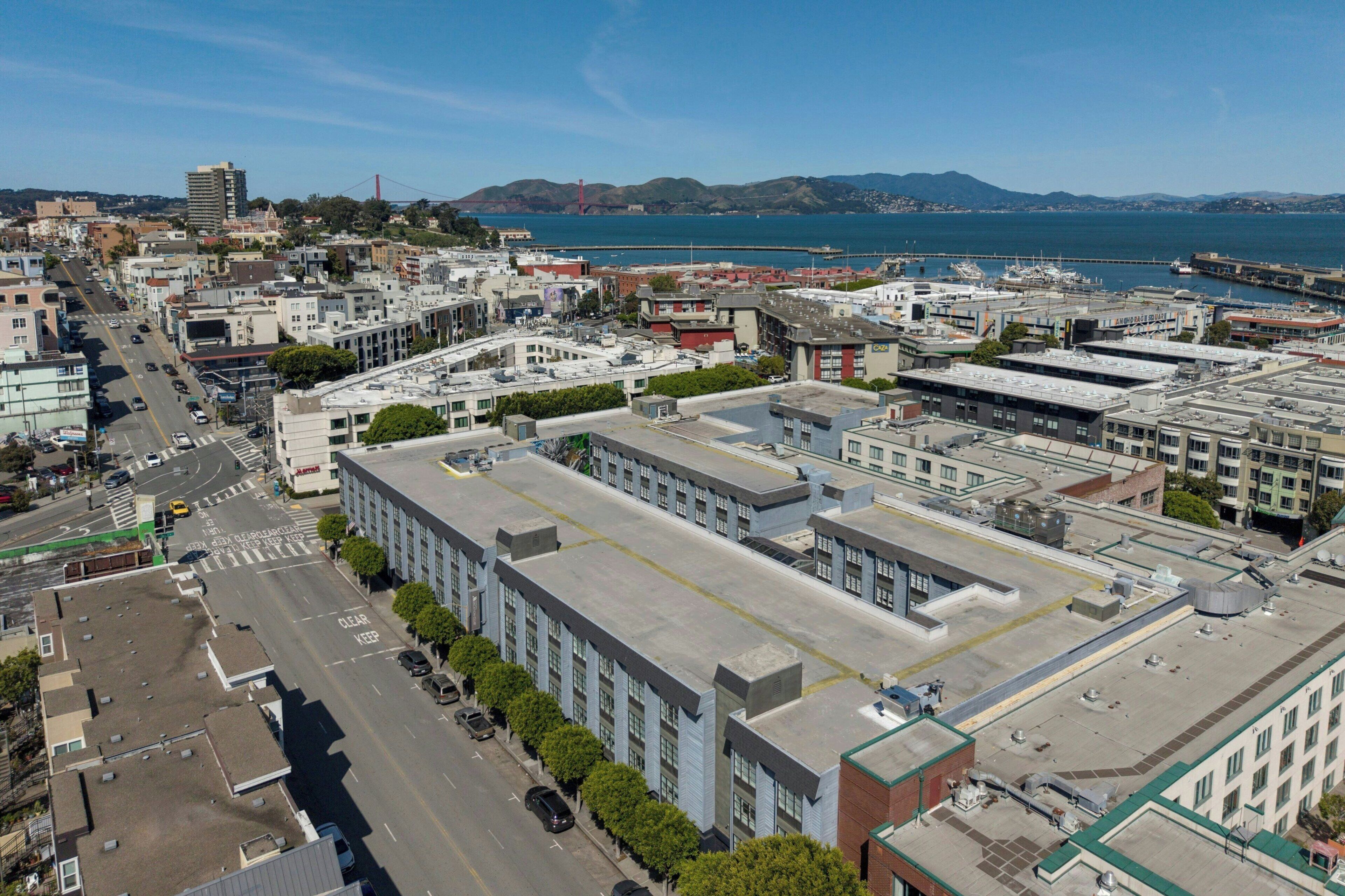 An aerial view of a cityscape with a prominent building featuring a flat roof and multiple windows.