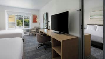 A hotel room with a bed, a desk with a TV, a chair, and a window with blinds.