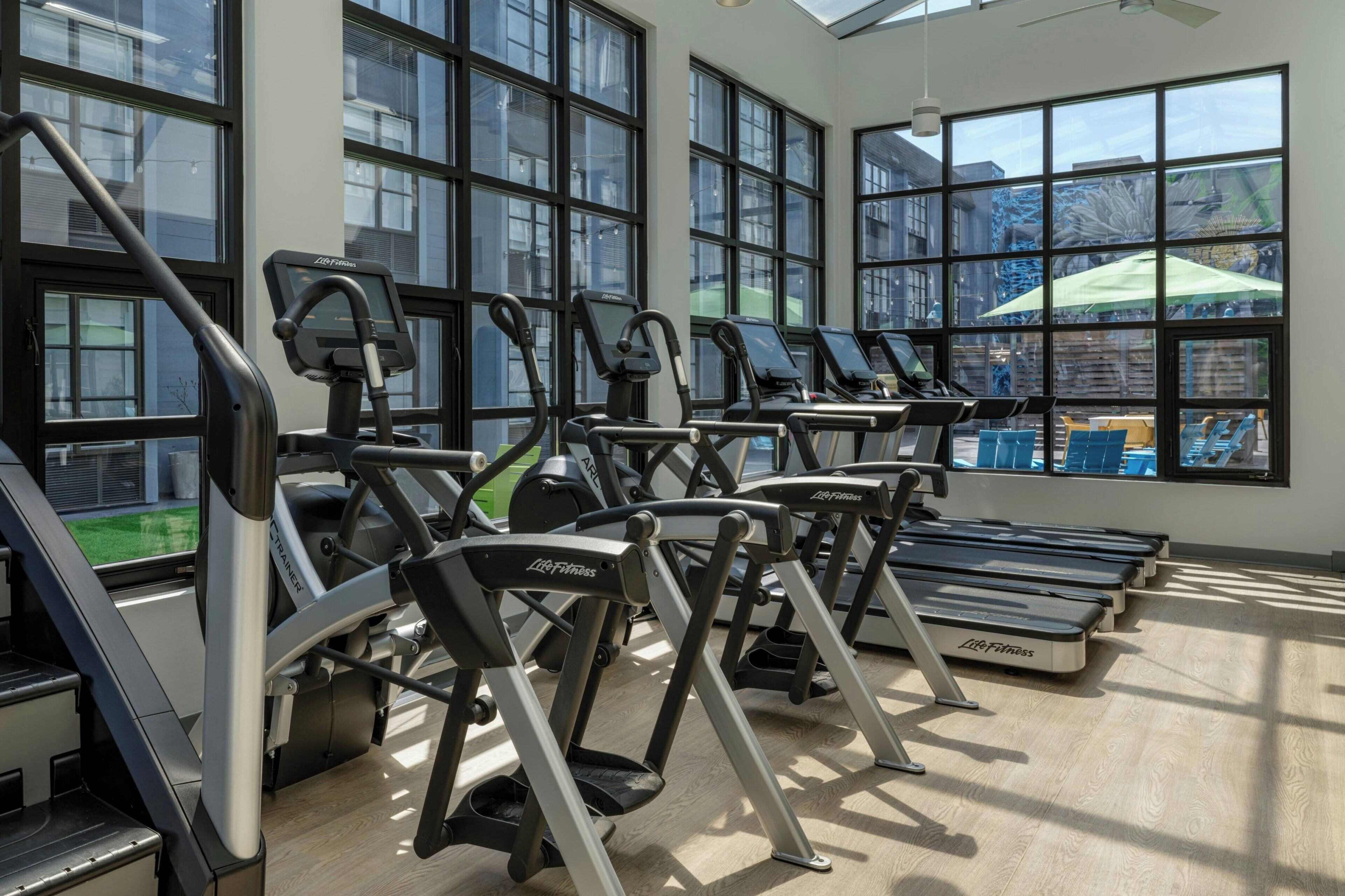 Un gimnasio con cintas de correr y bicicletas estáticas, ventanas amplias y vistas al exterior.