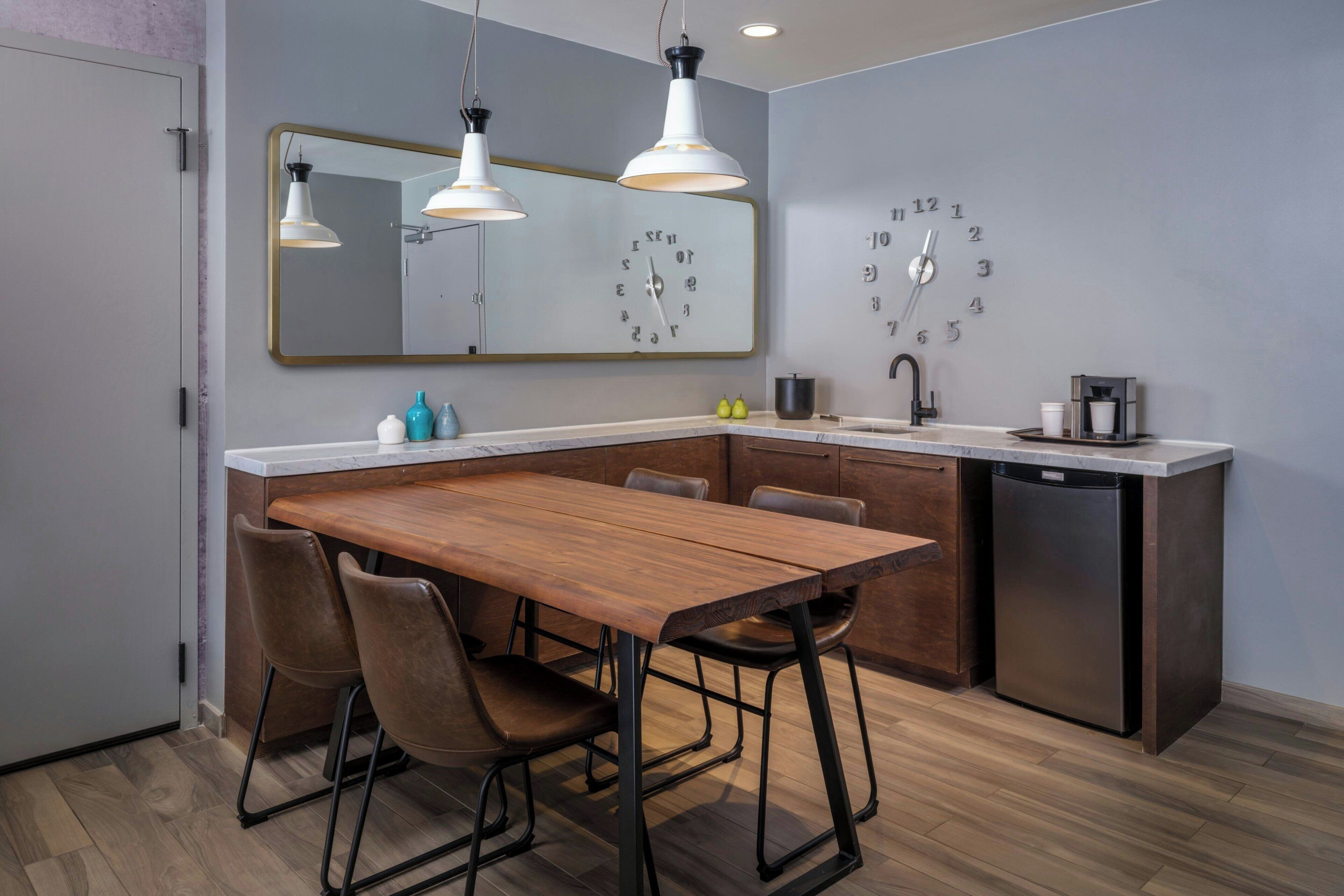 Une cuisine moderne avec une table à manger en bois, des chaises, un lave-vaisselle encastré et une horloge murale.