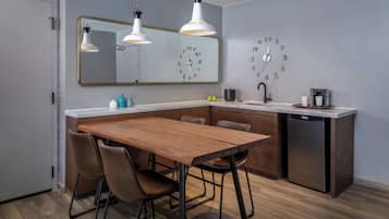 Uma cozinha moderna com uma mesa de jantar de madeira, cadeiras, máquina de lavar louça embutida e um relógio de parede.
