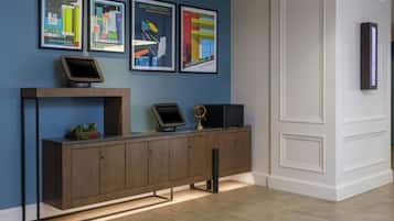 A reception desk with a digital screen, a small plant, and a framed poster of a cityscape.