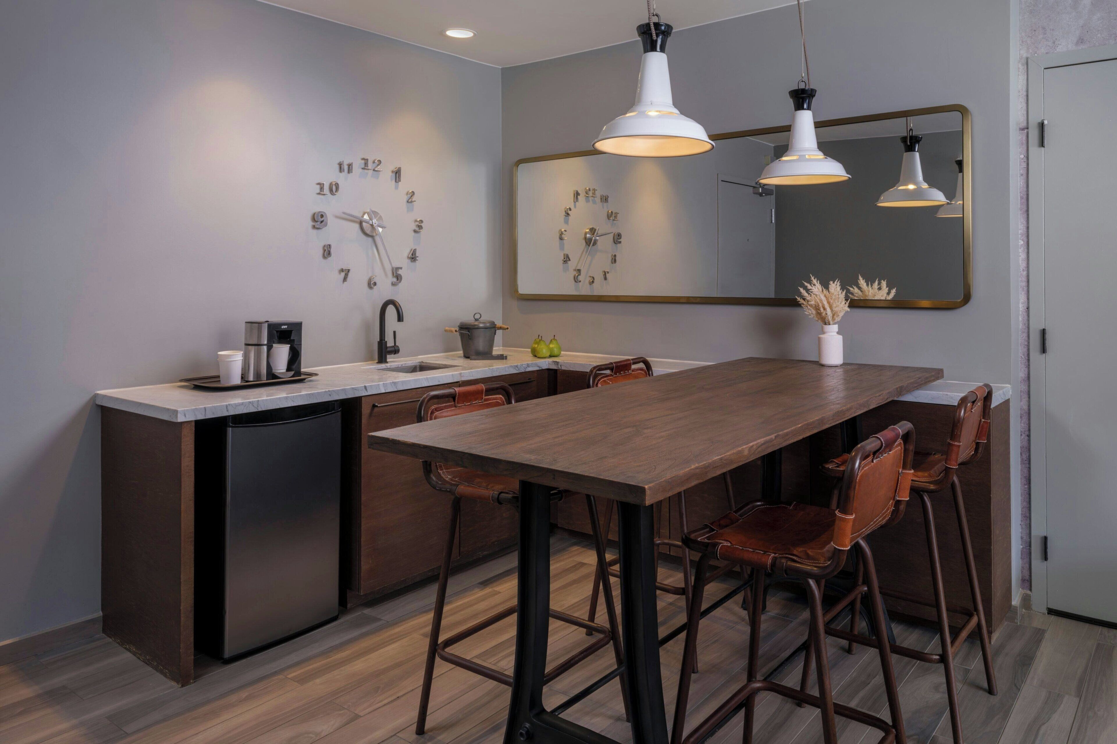 A modern kitchen with a central island, bar stools, a coffee machine, and a clock on the wall.