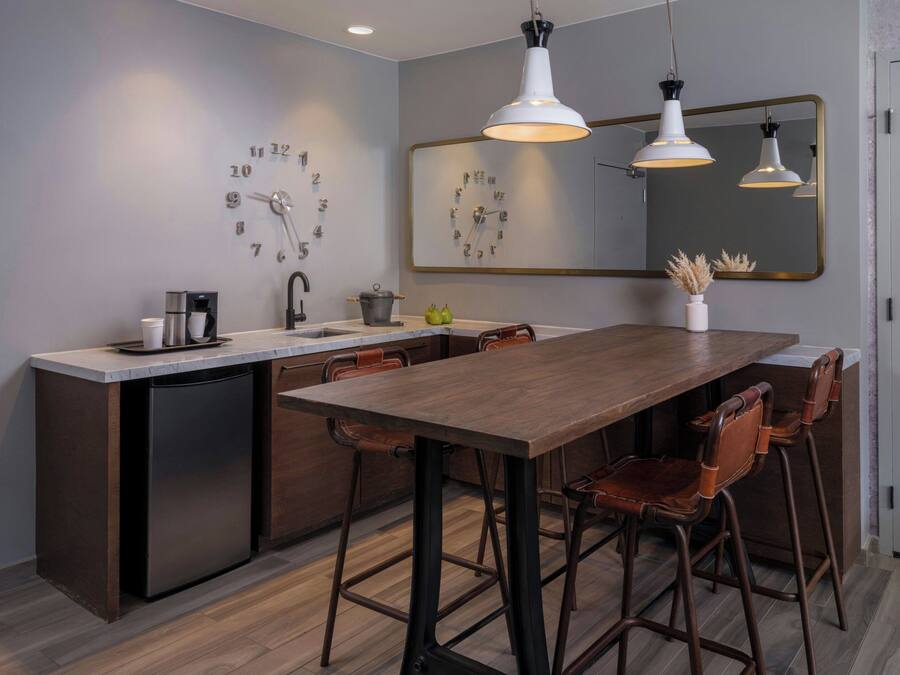 A modern kitchen with a central island, bar stools, a coffee machine, and a clock on the wall.