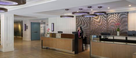 A modern reception area with a wooden reception desk, a patterned wall, and a large mirror.
