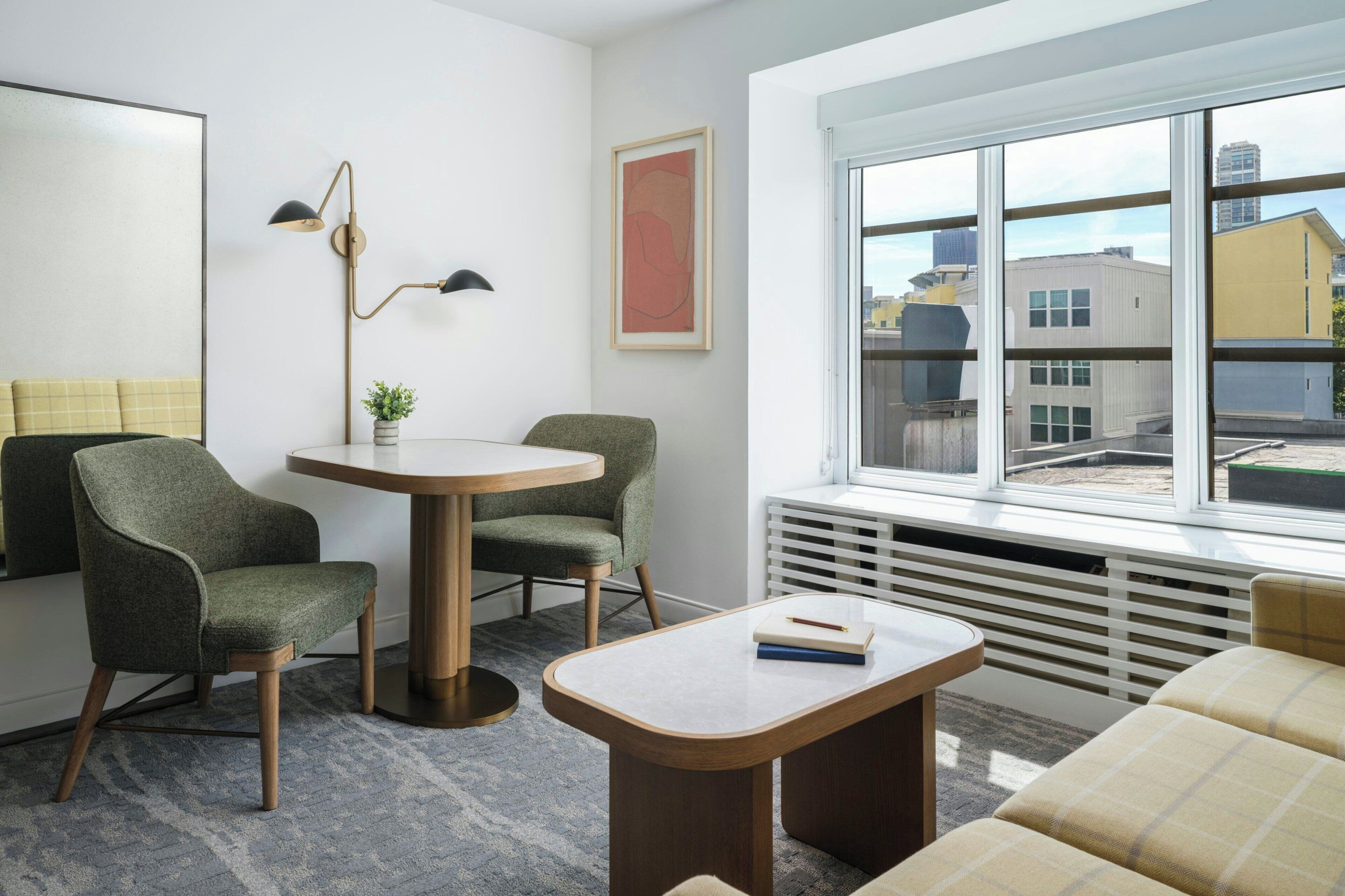 A modern living room with a round table, two armchairs, a sofa, a radiator, and a window with a city view.