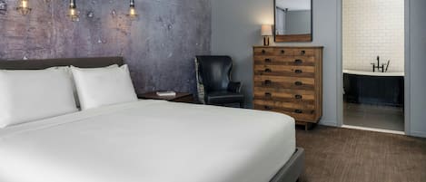 A bedroom with a large bed, a wooden dresser, a chair, a mirror, and a bathroom with a white sink.