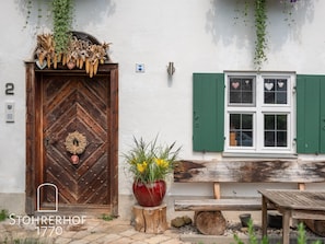 A traditional wooden door with a decorative wreath, a green window with shutters, and a wooden bench outside. - Gut Stohrerhof (Dießen am Ammersee)