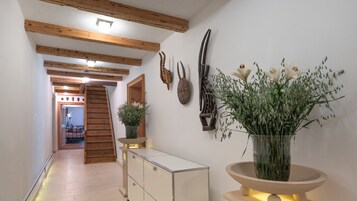 Um corredor com vigas de madeira, escadaria, armário e um vaso com flores.