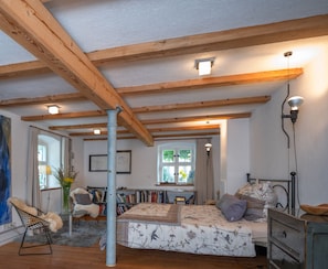 Ein Schlafzimmer mit Holzboden, einem Bett mit floralem Bettzeug, einem Schreibtisch mit Stuhl und einem Bücherregal.