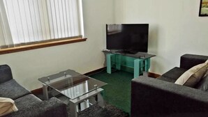 A living room with a flat-screen TV on a stand, a glass coffee table, and two grey sofas.
