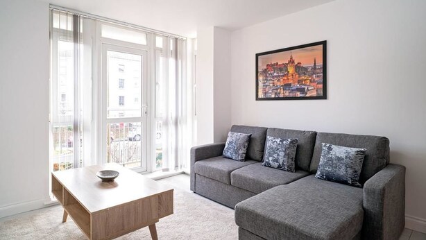 Ein Wohnzimmer mit grauem Sofa, einem Holztisch und einem Stadtbild an der Wand.