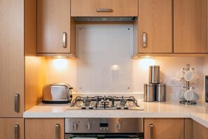 A modern kitchen with wooden cabinets, a stainless steel gas stove, a toaster, and a coffee maker.